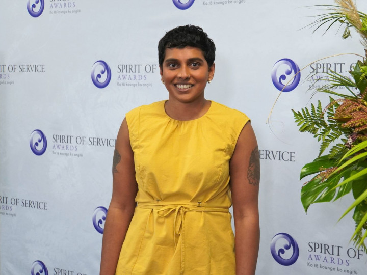 Gayathiri Ganeshan standing in front of awards banner and smiling at the camera