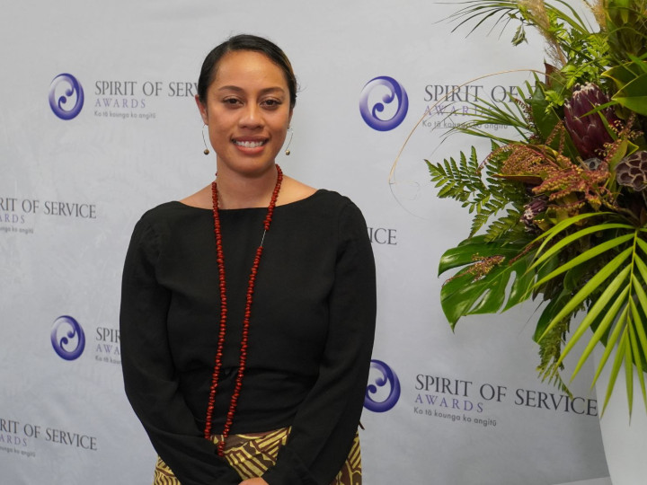 Mary Soonaoso Tiumalu standing in front of awards banner and smiling at the camera