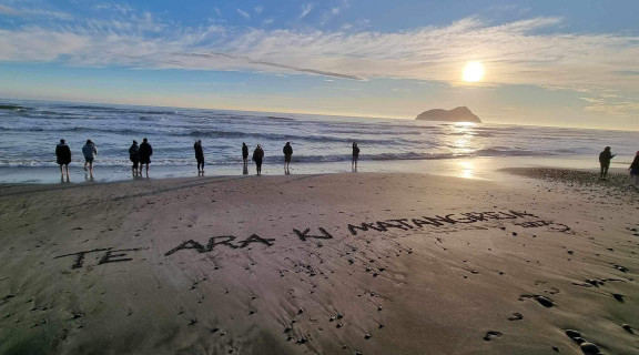 The 2023 cohort standing on the beach with 'Te Ara ki Matangireia' etched in the sand