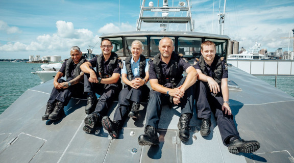Group of border patrol workers in uniform sitting on the front of a boat and smiling at the camera