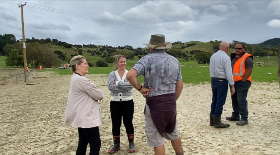 Darlene Rastrick standing on a flood affected farm speaking with the Rural Support Trust and local farmers