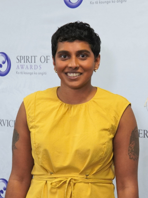 Gayathiri Ganeshan standing in front of awards banner and smiling at the camera