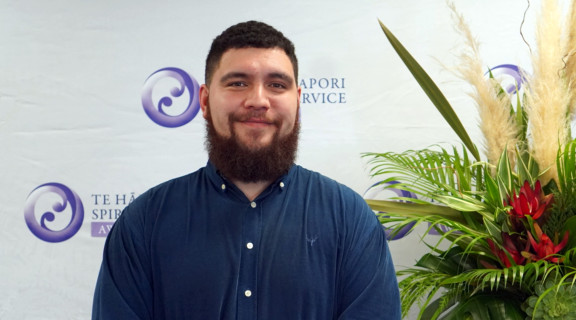 Jacob McGregor standing in front of awards banner and smiling at the camera