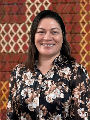 Jules Lynch standing in front of a tukutuku panel looking at the camera and smiling