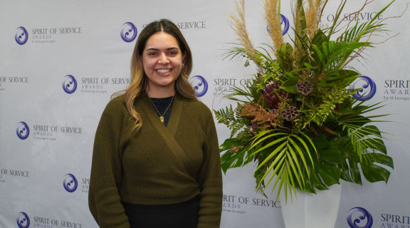 Kiriana Haze standing in front of awards banner and smiling at the camera