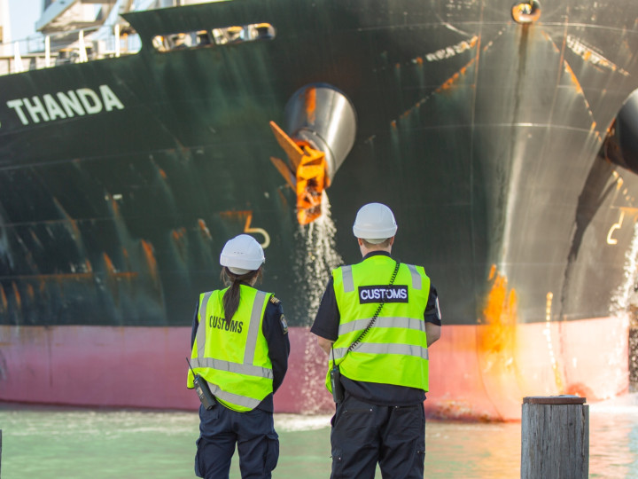 NZ Customs two Customs officers looking at boat coming into harbour captioned