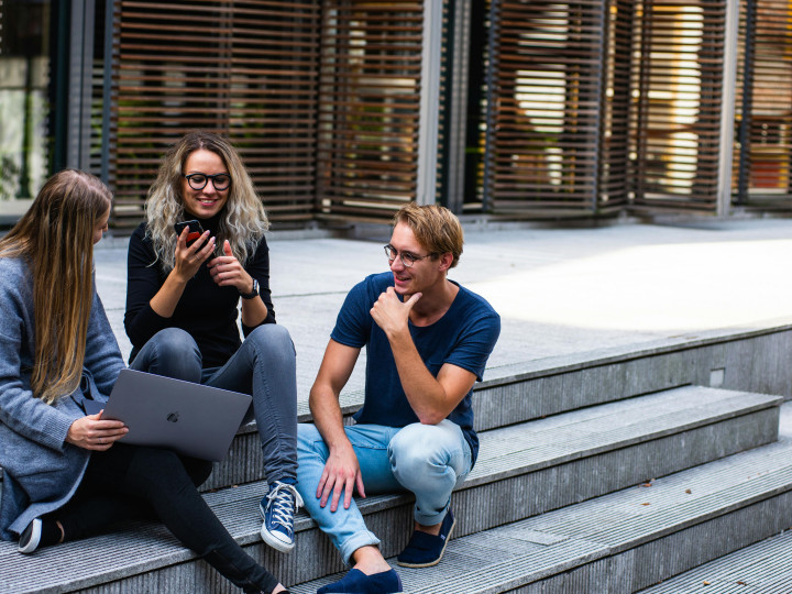Three people sitting on steps looking at a laptop and talking