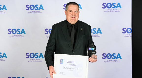 Paul Woodgate standing in front of the SOSA banner smiling at the camera