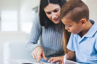 A woman is helping a child to read a book.