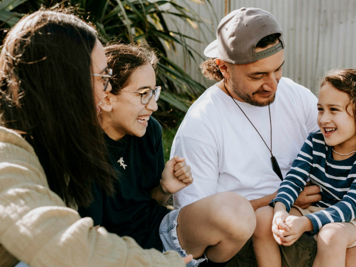 A mother, father and 2 young girls sitting together and laughing