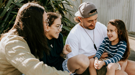 A mother, father and 2 young girls sitting together and laughing