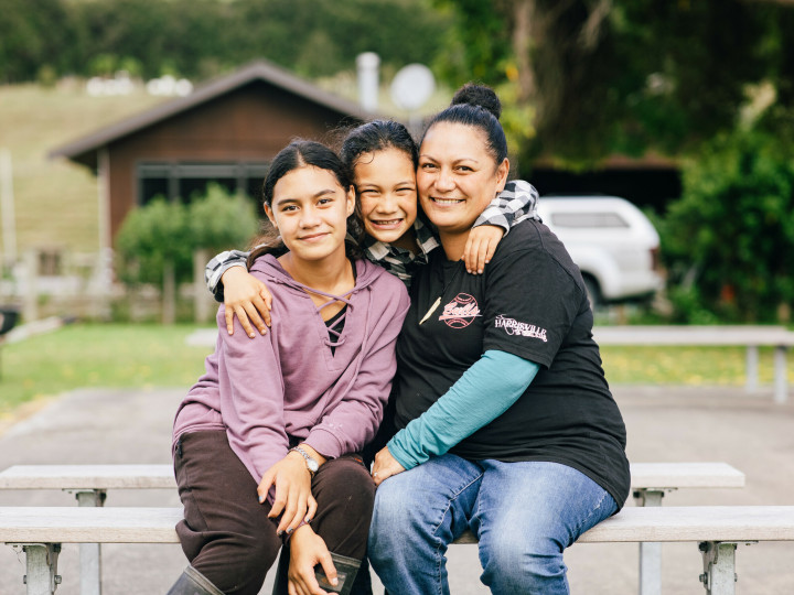 A mother with 2 young girls sitting together looking at the camera and smiling