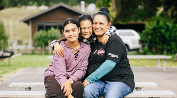 A mother with 2 young girls sitting together looking at the camera and smiling