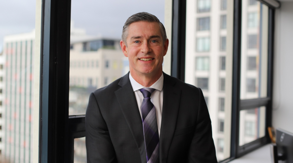 Andrew Coster standing in an office looking at the camera and smiling