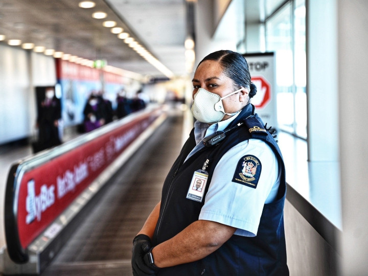 NZ Customs officer wearing uniform and a facemask is standing in an airport
