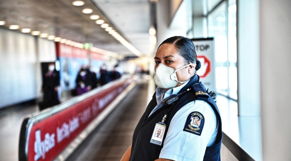 NZ Customs officer wearing uniform and a facemask is standing in an airport