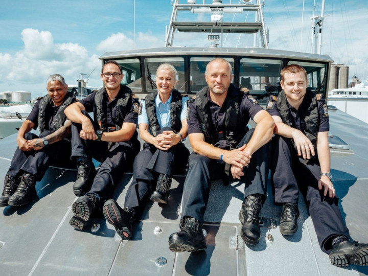 Group of border patrol workers in uniform sitting on the front of a boat and smiling at the camera