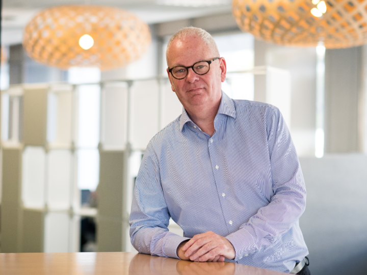 Peter Hughes standing at a table looking at the camera and smiling