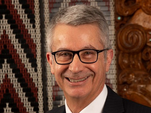 Bede Corry standing in front of a tukutuku panel looking at the camera and smiling