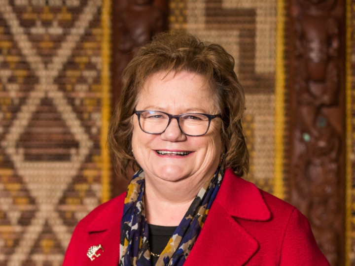 Gloria Campbell standing in front of a tukutuku panel looking at the camera and smiling