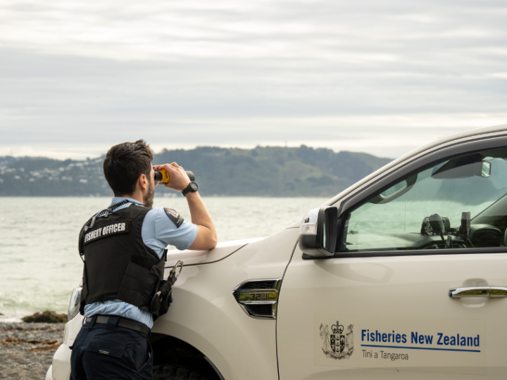 Fisheries Officer leaning on bonnet of 4 wheel drive, looking through a pair of binoculars