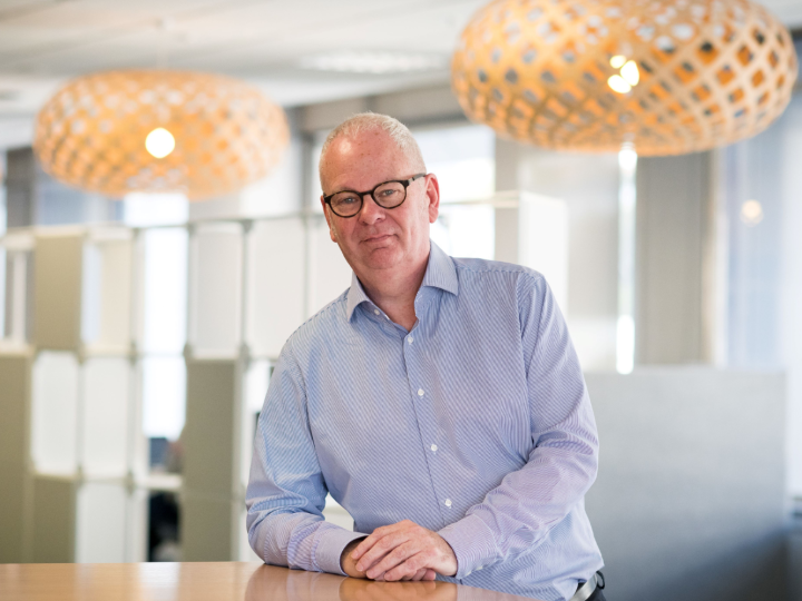 Peter Hughes standing at a table looking at the camera and smiling